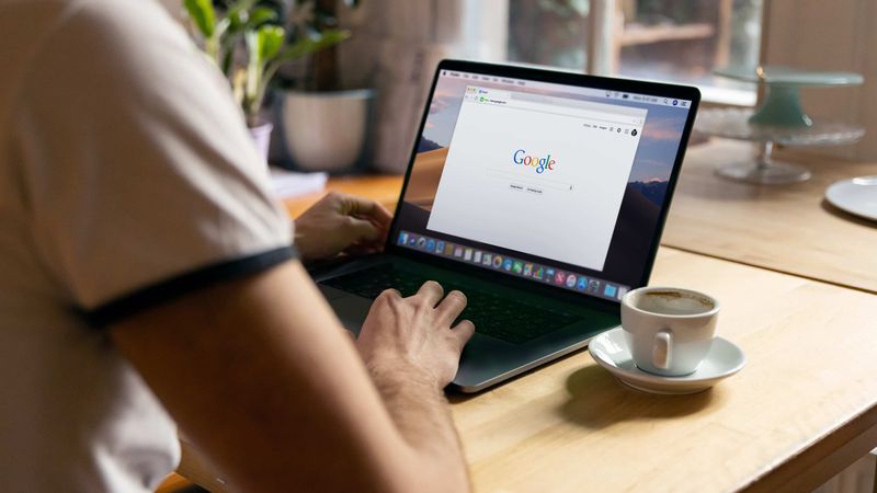 Ein Mann von hinten, der seinen Apple MacBook-Laptop in einem Café verwendet, wobei die Google-Suchwebsite im Chrome-Browser angezeigt wird
