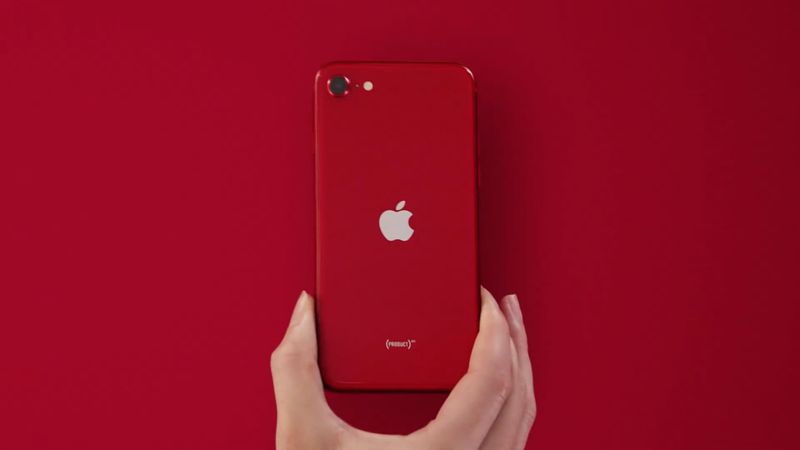 Eine Hand, die ein rotes iPhone SE 2 hält, vor einem komplett roten Hintergrund